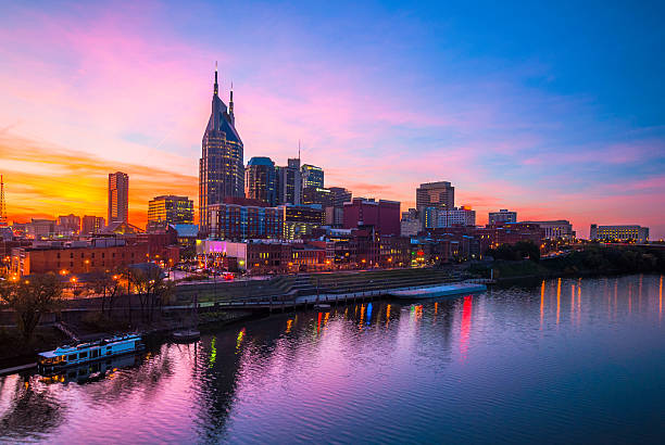 Nashville at Dusk with Beautiful Sky and Water Downtown Nashville skyline with a beautiful pink, orange, and blue sunset, with the blue and pink of the sky reflected on the Cumberland River. nashville stock pictures, royalty-free photos & images