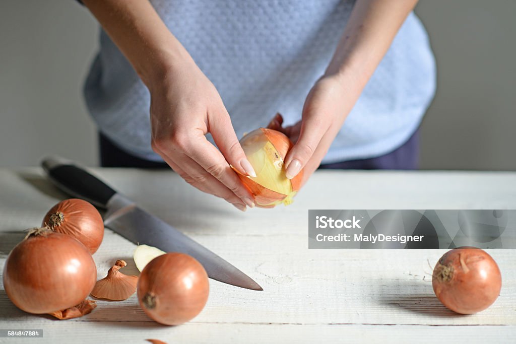 Woman hand peel fresh onion on white table Adult Stock Photo