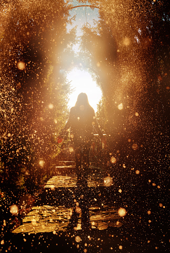 rear view of woman silhouette looking at the light from the end of the tunnel, being surrounded by shiny golden lights.