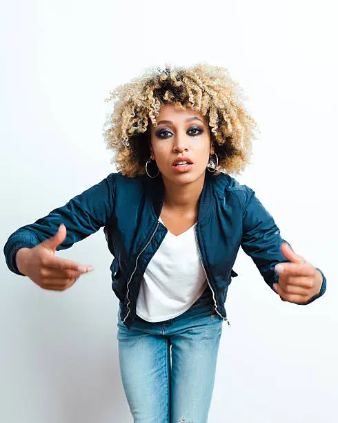 Portrait of afro american young woman wearing bomber jacket, denim trausers, looking at camera.