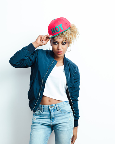 Portrait of afro american young woman wearing bomber jacket, denim trausers and pink baseball cap, looking at camera.