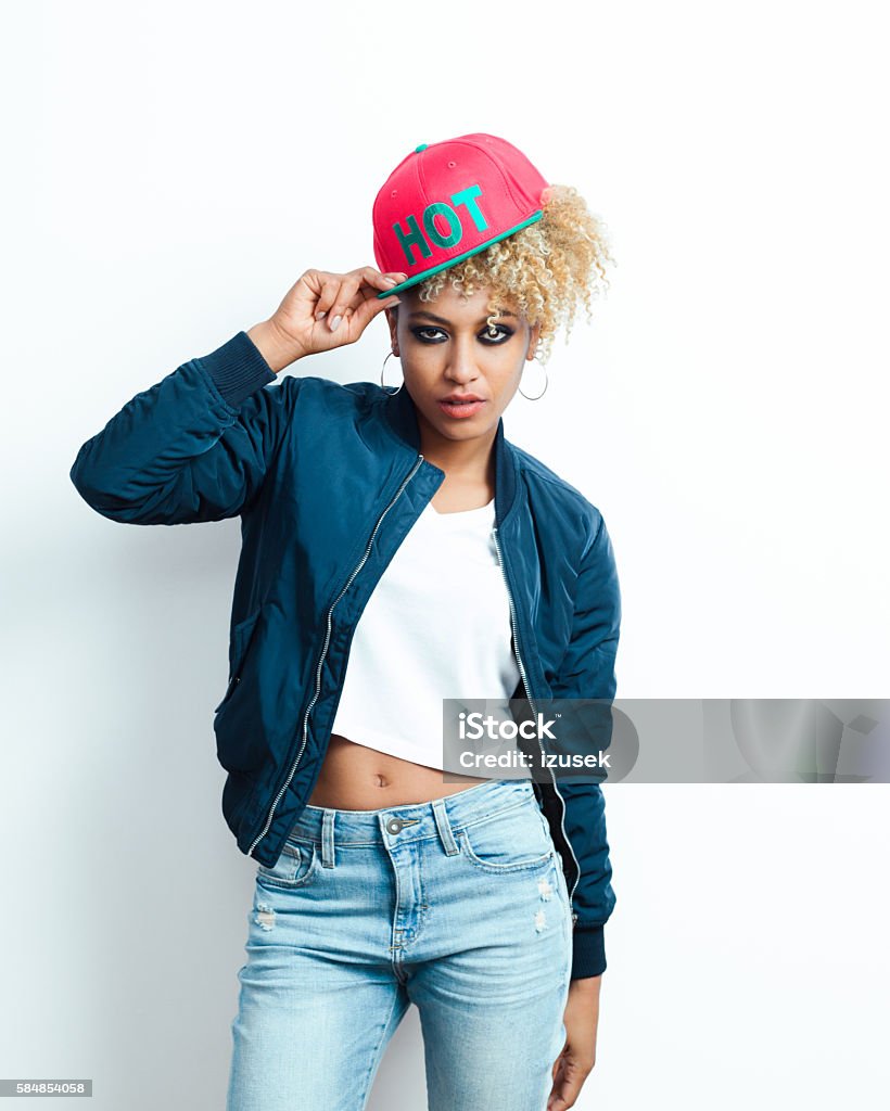 Portrait of afro american young woman with pink cap Portrait of afro american young woman wearing bomber jacket, denim trausers and pink baseball cap, looking at camera. Hip Hop Music Stock Photo