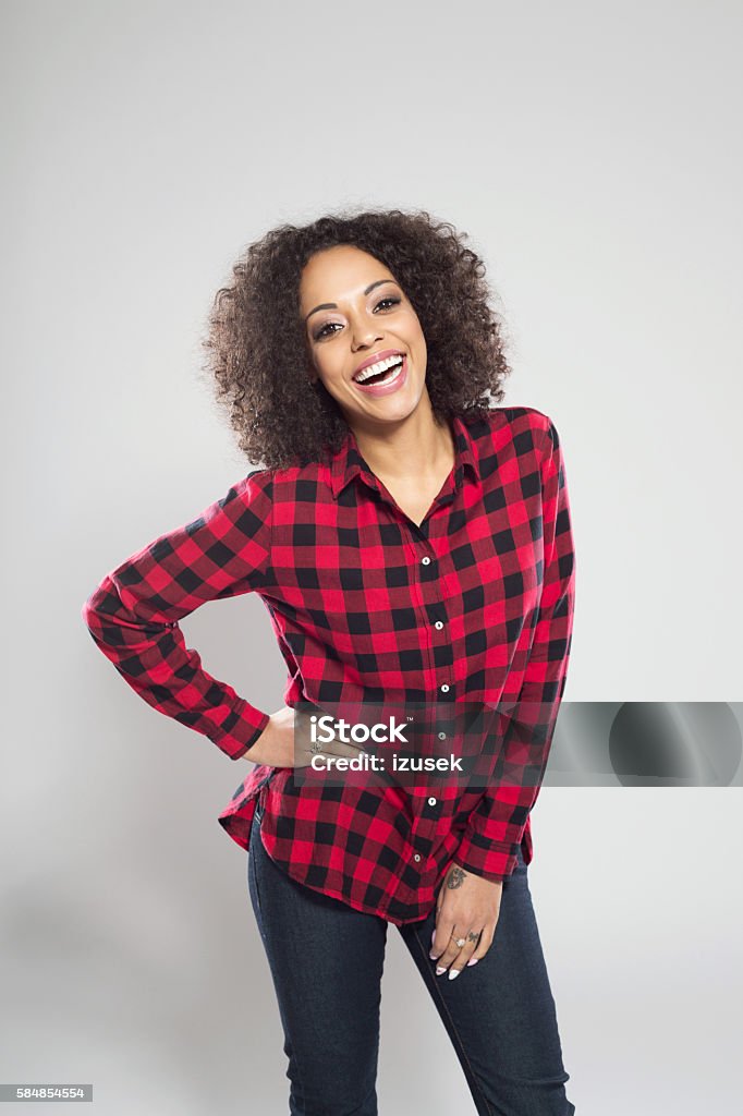Portrait of beautiful afro american young woman Portrait of beautiful afro american young woman wearing casual red checkered shirt, standing against grey background and laughing at camera. Adult Stock Photo