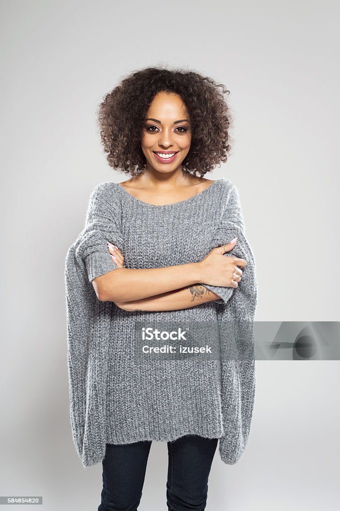 Portrait of beautiful afro american young woman Portrait of beautiful afro american young woman wearing casual wool sweater, standing against grey background and smiling at camera. Adult Stock Photo