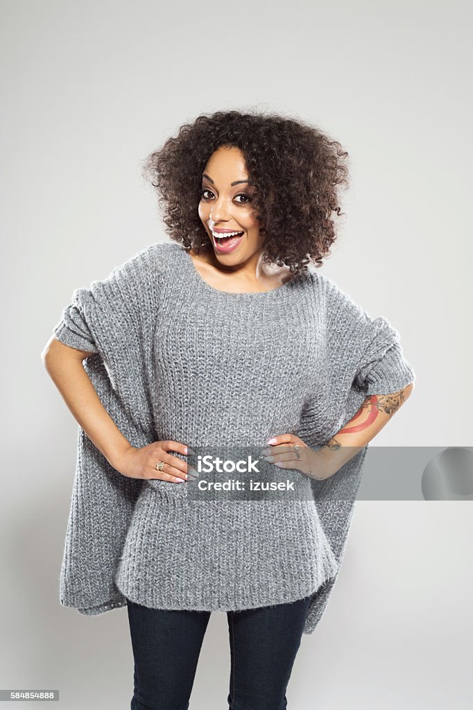 Portrait of surprised afro american young woman Portrait of surprised afro american young woman wearing casual wool sweater, standing against grey background and laughing at camera. Adult Stock Photo