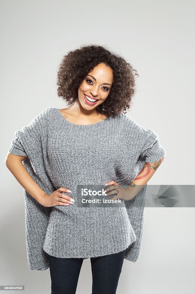 Portrait of successful afro american young woman Portrait of beautiful afro american young woman wearing casual wool sweater, standing against grey background and smiling at camera. Adult Stock Photo