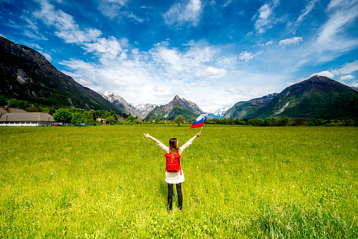 Beautiful landscape with mountains, green field and woman holding slovenian flag. Traveling in Triglav national park in Slovenia