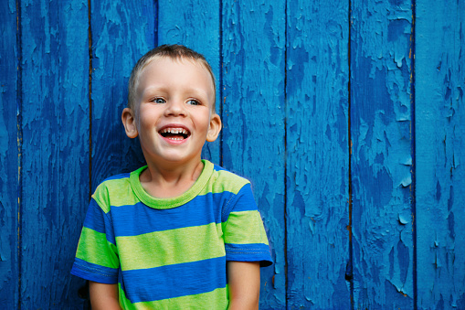 Portrait of happy joyful beautiful little boy against the old textured blue wall