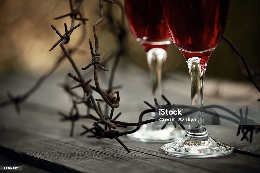 Wine in glasses and a barbed wire. Glasses with alcoholic drink and a rusty barbed wire on a wooden table. Alcoholic dependence. Abstract Stock Photo