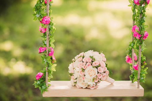 wedding bouquet of beige and pink roses outdoors on the decorated swing