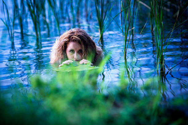 istock Red-haired female hiding behind lily pads in water 584876966