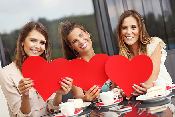 istock Three girlfriends holding hearts in cafe 584879830