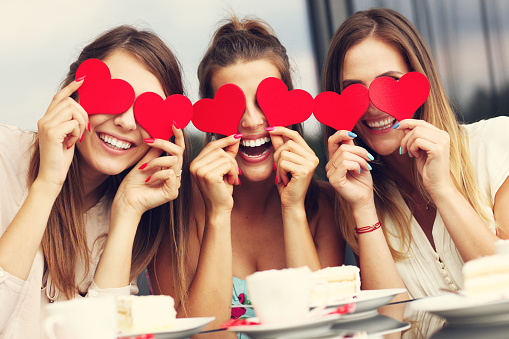 Picture presenting three girlfriends holding hearts in cafe