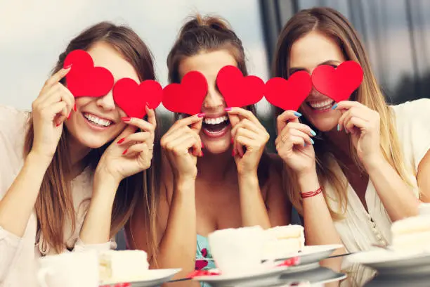 Photo of Three girlfriends holding hearts in cafe