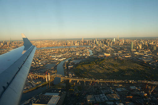 Flying across a bridge of New York City from east side of the island. Midtown skyline is visible as far end background while one of the wing of the airplane is approaching the destination in the air.