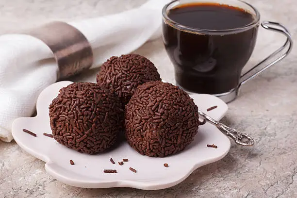Brazilian chocolate truffle bonbon brigadeiro on plate with cup of coffee on marble table. Selective focus