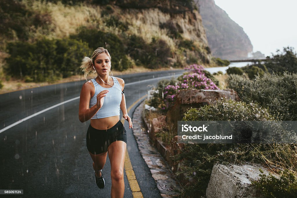 Fitness woman running on highway Fitness woman running on highway around the mountains. Female athlete training outdoors during rain. Running Stock Photo