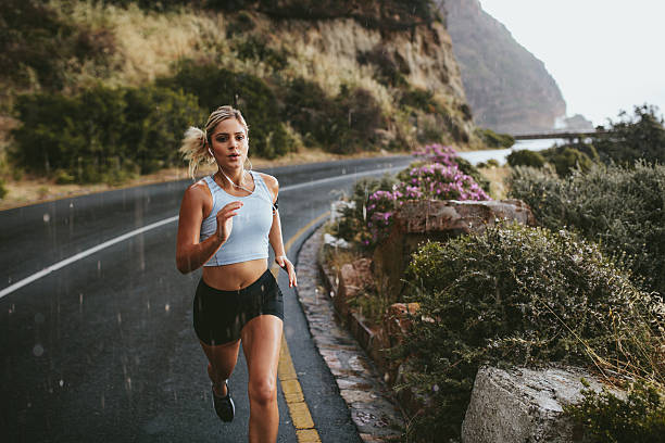 Fitness woman running on highway Fitness woman running on highway around the mountains. Female athlete training outdoors during rain. track event photos stock pictures, royalty-free photos & images