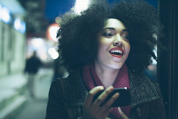 istock Smiling young african woman using phone on street by night 585051204