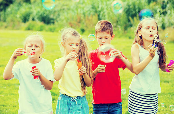 istock Four  kids sitting together and blowing soap bubbles 585054896