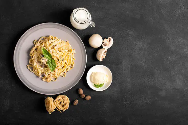 Pasta with mushrooms and bechamel sauce. Ingredients for spaghetti on a black background.  Copy space for your text