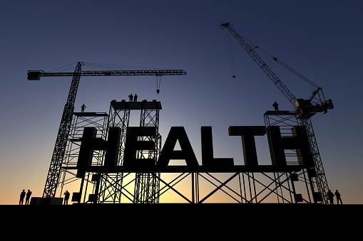 Backlit silhouette of a construction site with cranes and steel structures building the word health