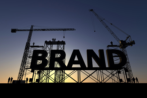 Backlit silhouette of a construction site with cranes and steel structures building the word brand