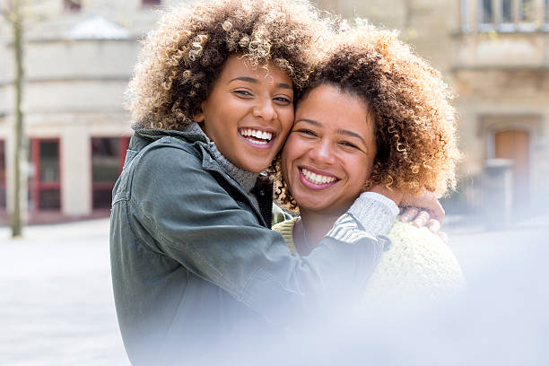 Sisters in the City Two friends hugging and smiling for the camera in the city. sister stock pictures, royalty-free photos & images