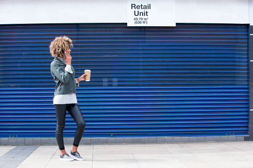 Young woman enquiring about a retail unit on the phone. She is dressed casually and is holding a disposable coffee cup.