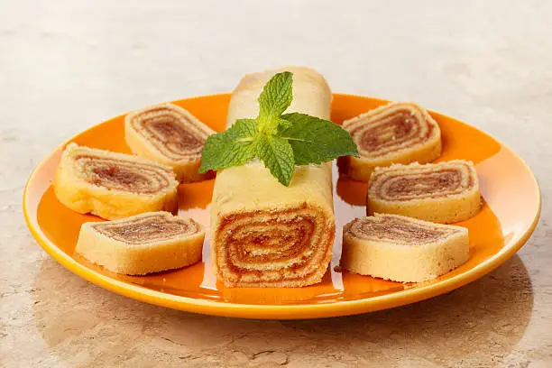 Bolo de rolo (swiss roll, roll cake) Brazilian dessert on orange plate on marble table. Selective focus