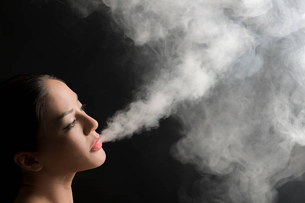 istock Beautiful woman blowing vape smoke. 585152504