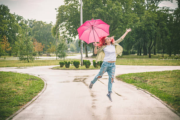 happy young woman jumping with umbrella - women jumping bouncing spring imagens e fotografias de stock