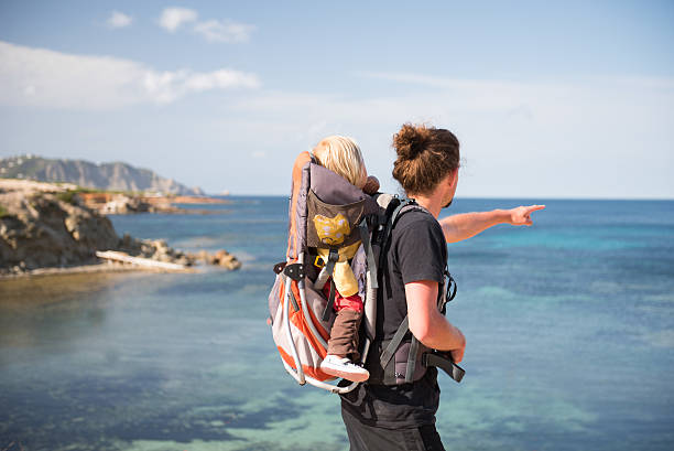 Father and baby in backpack carrier outdoors near the sea stock photo