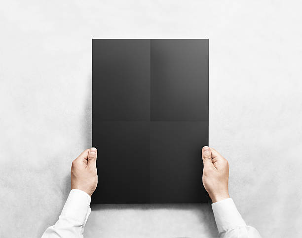 istock Hand holding black folded blank poster mockup, isolated. 585157992