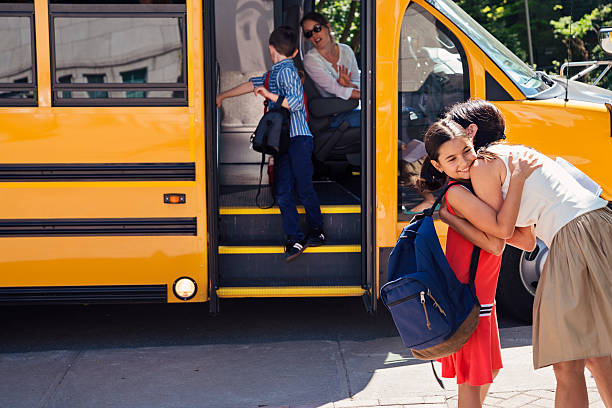 Mother greeting elementary age girl getting off school bus. Mother greeting elementary age girl getting off yellow school bus. Little boy saying goodbye to the driver in the background. Woman is driving the bus. Horizontal outdoors shot with copy space. This was taken in Quebec, Canada. disembarking stock pictures, royalty-free photos & images