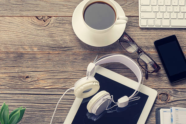 High angle shot of mobile devices and headphones. There are several smart phones and a digital tablet along with a keyboard. Devices are on a wooden table with coffee. Copy space on left