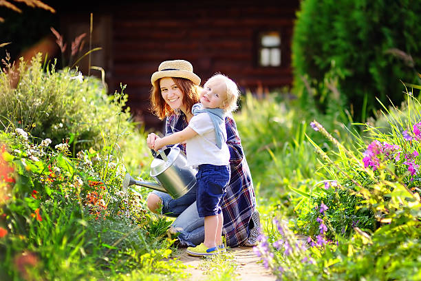 le petit garçon et sa mère arrosent des plantes dans le jardin - baby toddler child flower photos et images de collection