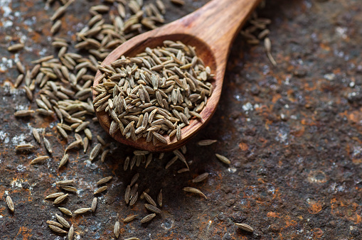 Cumin seeds in wooden spoon on texture background