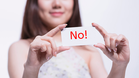 Half smiling face of young woman showing the white card with message No, selective focus on the card.