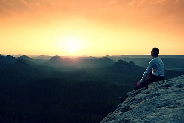 istock Man sit on peak. Colorful fog in forest valley 585173782