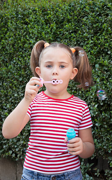 istock little girl blowing soap bubbles in summer park. 585174642