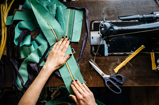 Overhead shot of hands of young female fashion designer with fabrics and scissor and an old sewing machine.