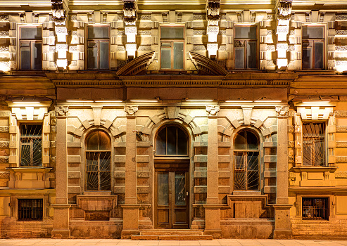 Several windows in a row and door on night illuminated facade of urban apartment building front view, St. Petersburg, Russia