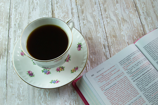 The Holy Bible opened to the book of Mark with a flowered tea cup filled with coffee or tea