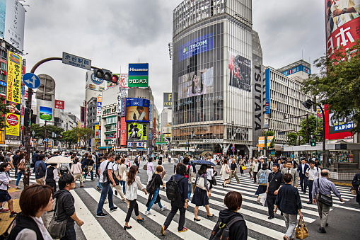 People crossing Shibuya crossing on a cloudy day.