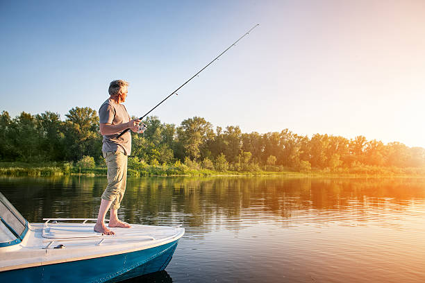 uomo maturo su una barca a motore. pesca - level rod foto e immagini stock