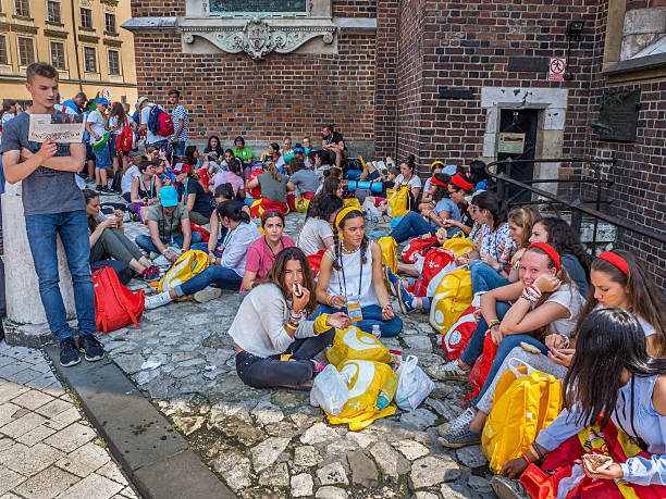 Krakow, Poland - July 29, 2016: World Youth Day 2016. Young pilgrims from various countries sitting on the ground, resting, eating and talking in groups in the shadow of st Mary church at the Market Square in Cracow.