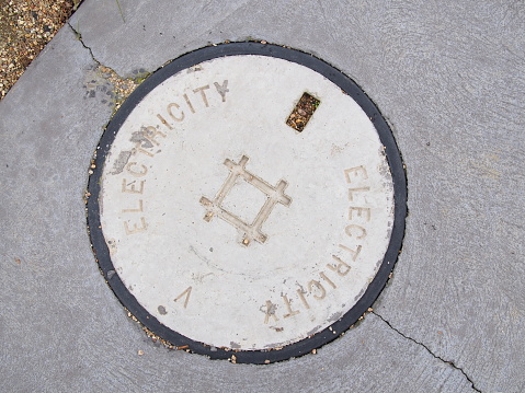 Round concrete lid on a electrical pit on a foot path marked with Electricity, Melbourne, Australia, 2016