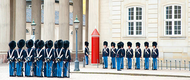 Copenhagen, Denmark - April 28, 2024: Two Royal Guards with rifles stand watch at Amalienborg Palace. The palace square and surrounding buildings create a historic backdrop.