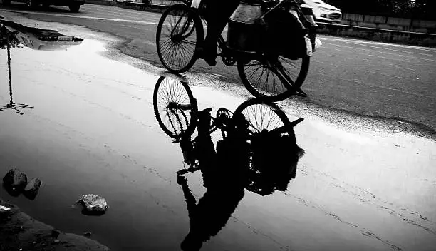 in India, monsoon waters get collected by the roadside and, at the golden hour, can work as a perfect reflector, perfectly reflecting the cyclist and the load he's carrying.